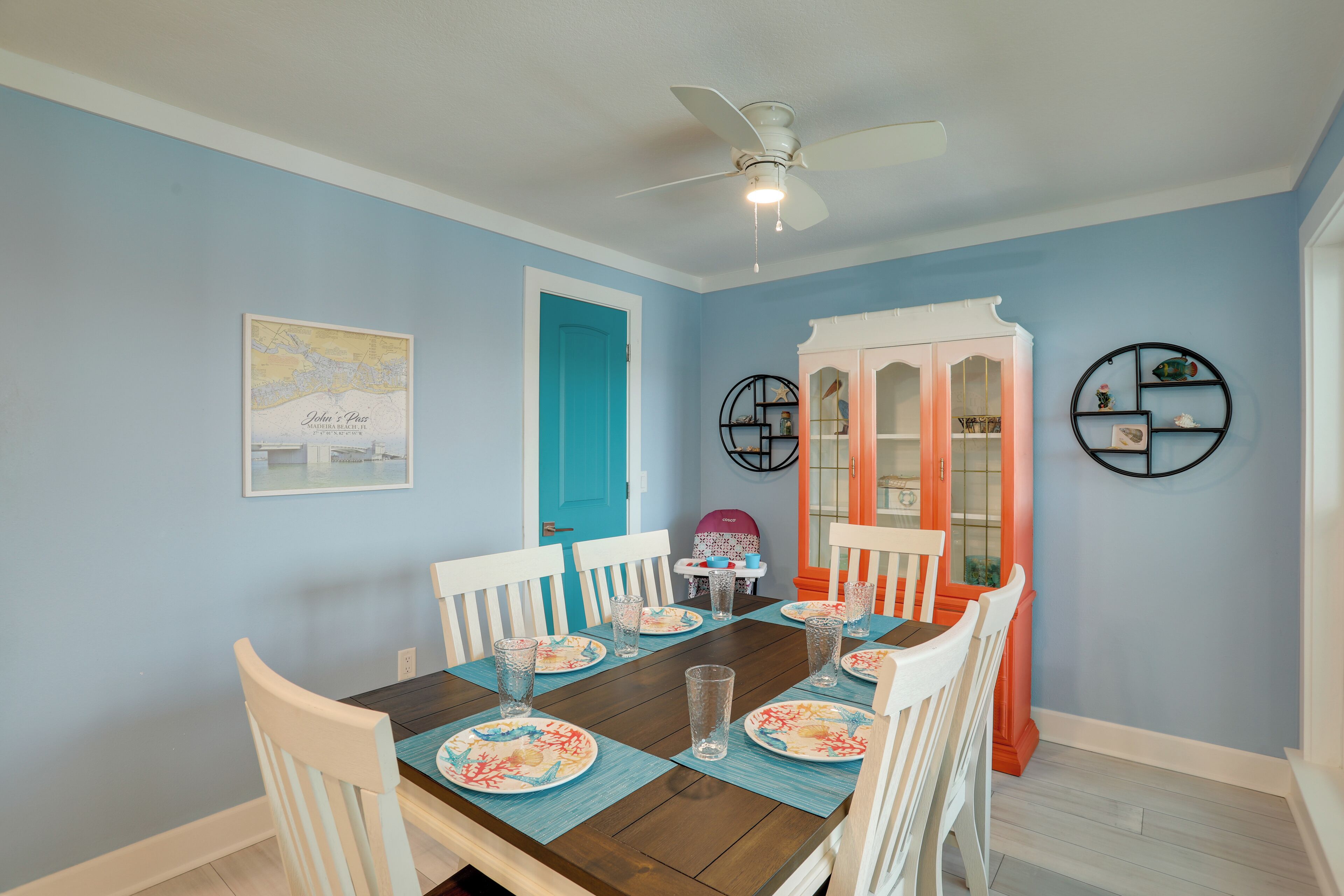 A dining area with a table set for four, chairs, a ceiling fan, and a wall with a framed map and decorative items.