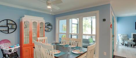 A dining area with a table set for four, surrounded by white chairs, a pink cabinet, and a ceiling fan.