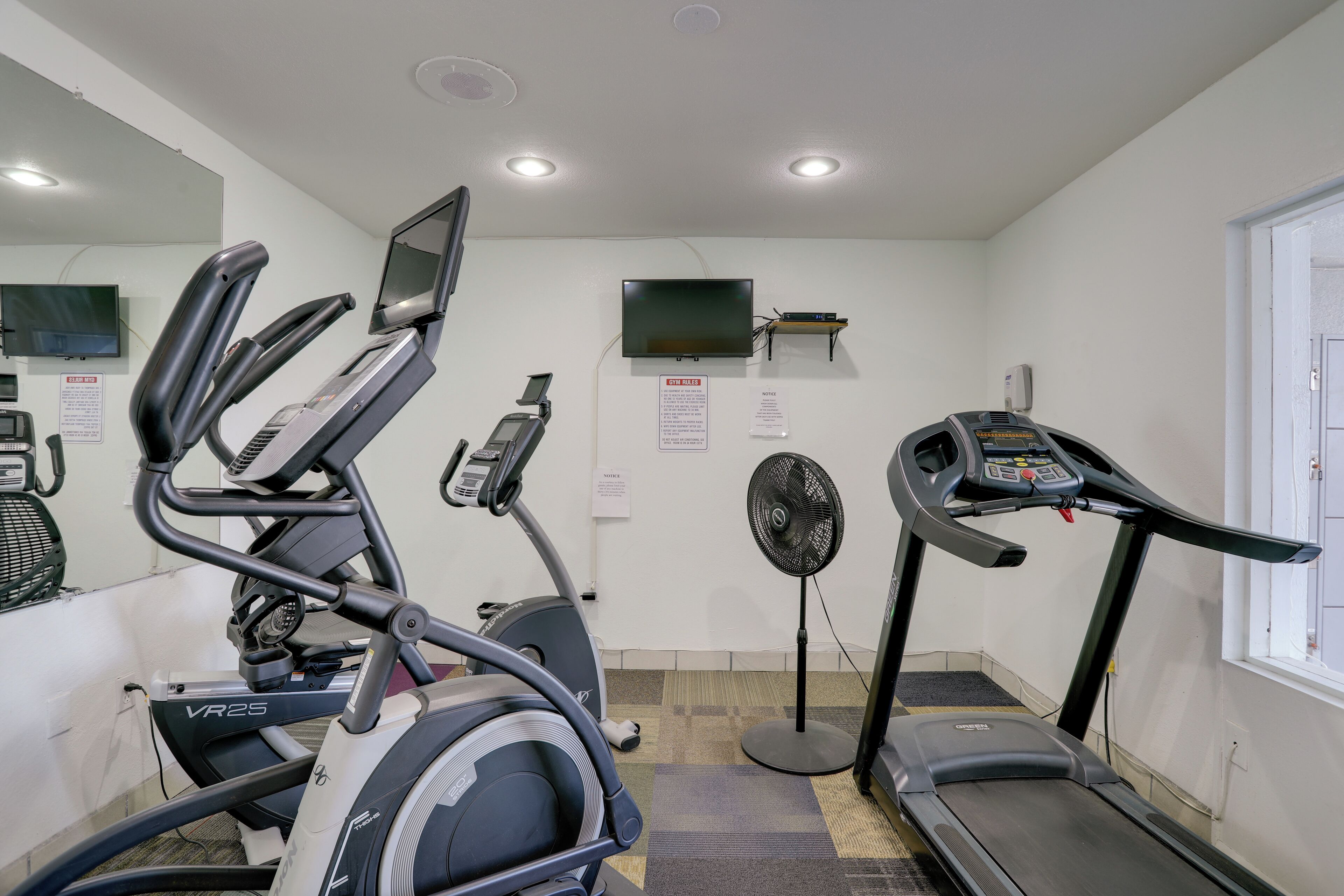 A gym with treadmills, an elliptical, a fan, and a TV on the wall.