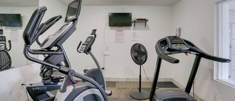 A gym with treadmills, an elliptical, a fan, and a TV on the wall.
