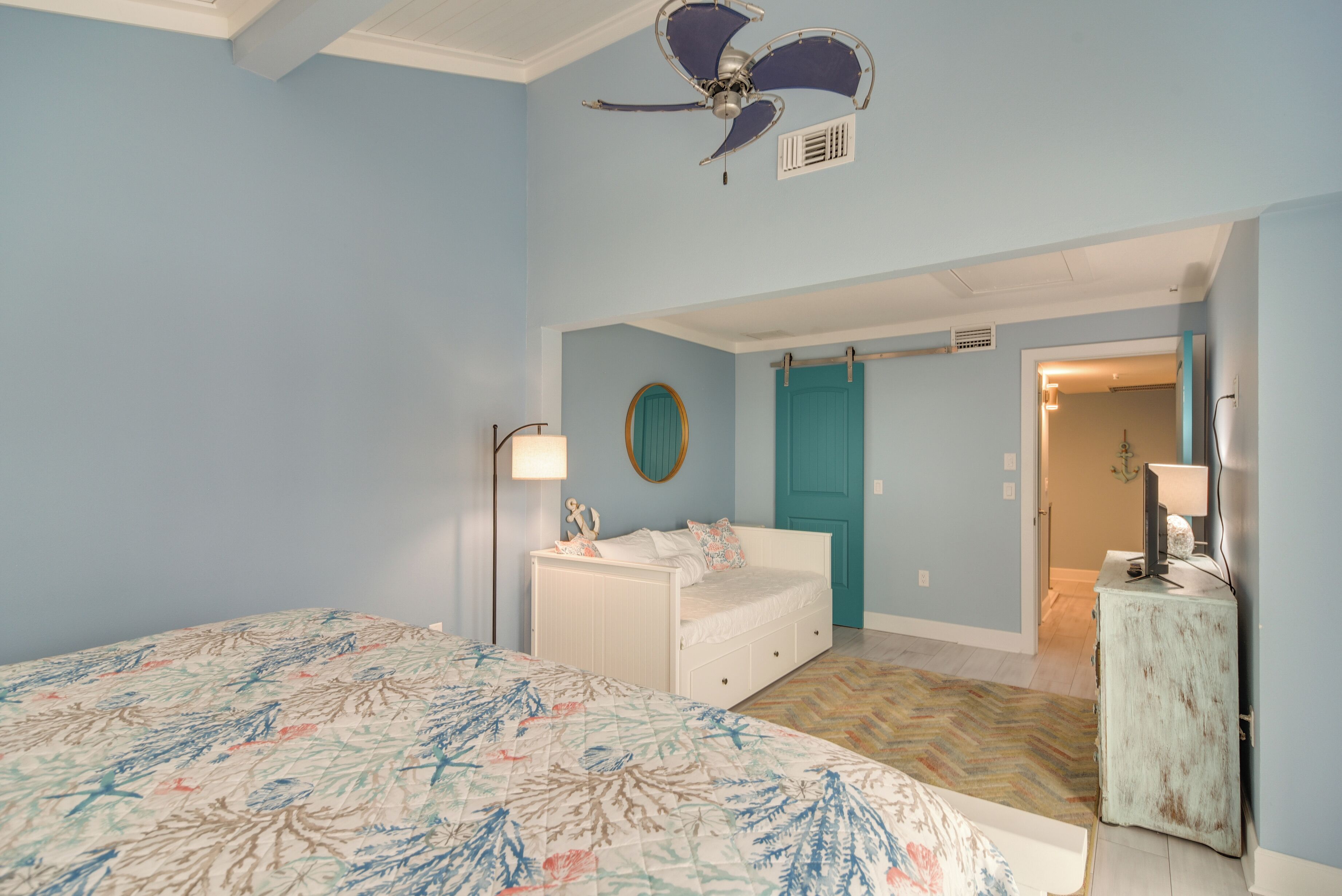 Een slaapkamer met een bed, een dressoir, een plafondventilator en een deur naar een andere kamer.