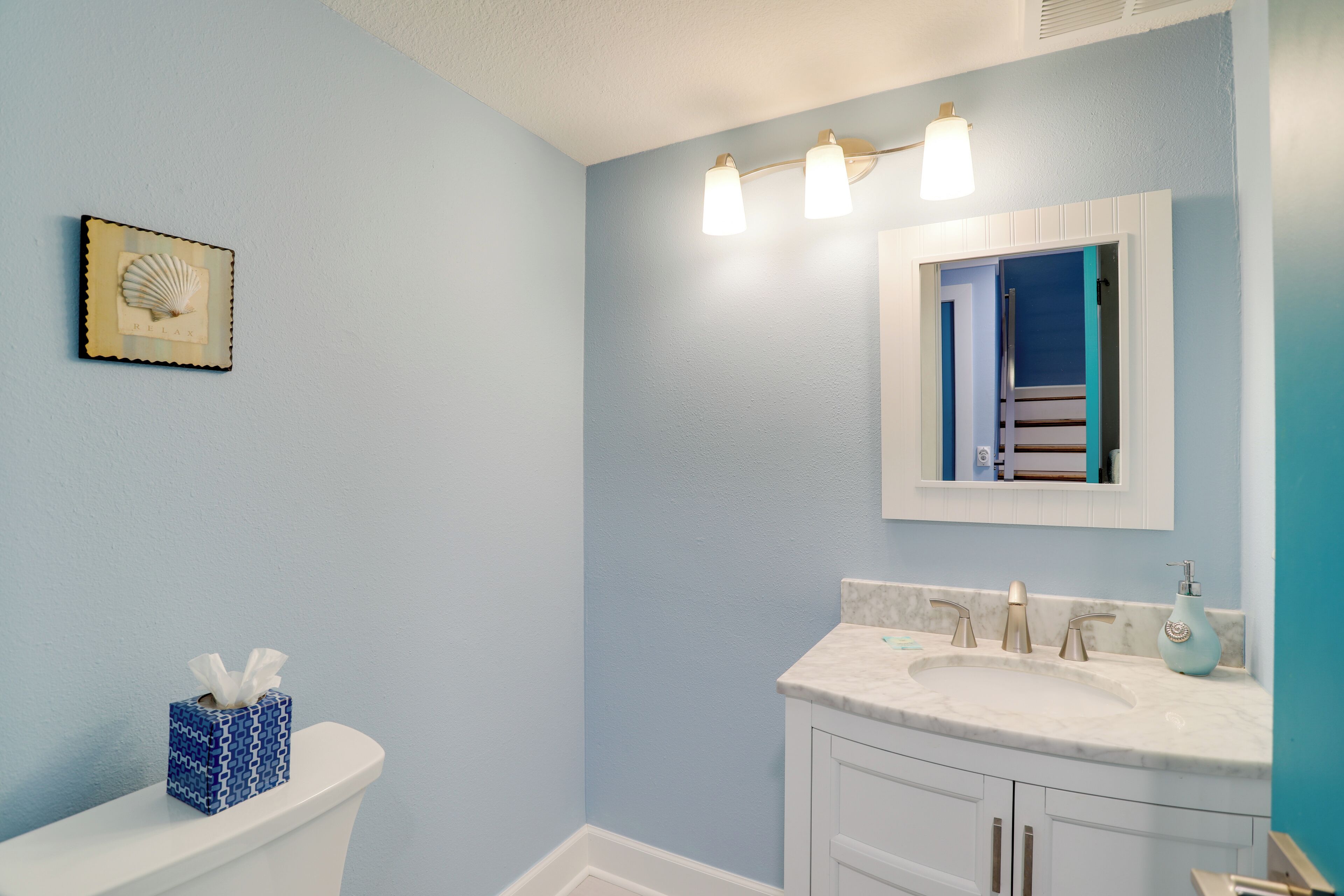 A bathroom with a toilet, a sink with a marble countertop, a mirror, and a towel rack.