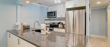 A modern kitchen with granite countertops, stainless steel appliances, and white cabinetry.
