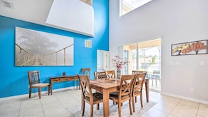 A dining area with a wooden table and chairs, a blue accent wall, and a large window. - Dog-friendly Kissimmee Home w/ Lanai + Pool! (Kissimmee)