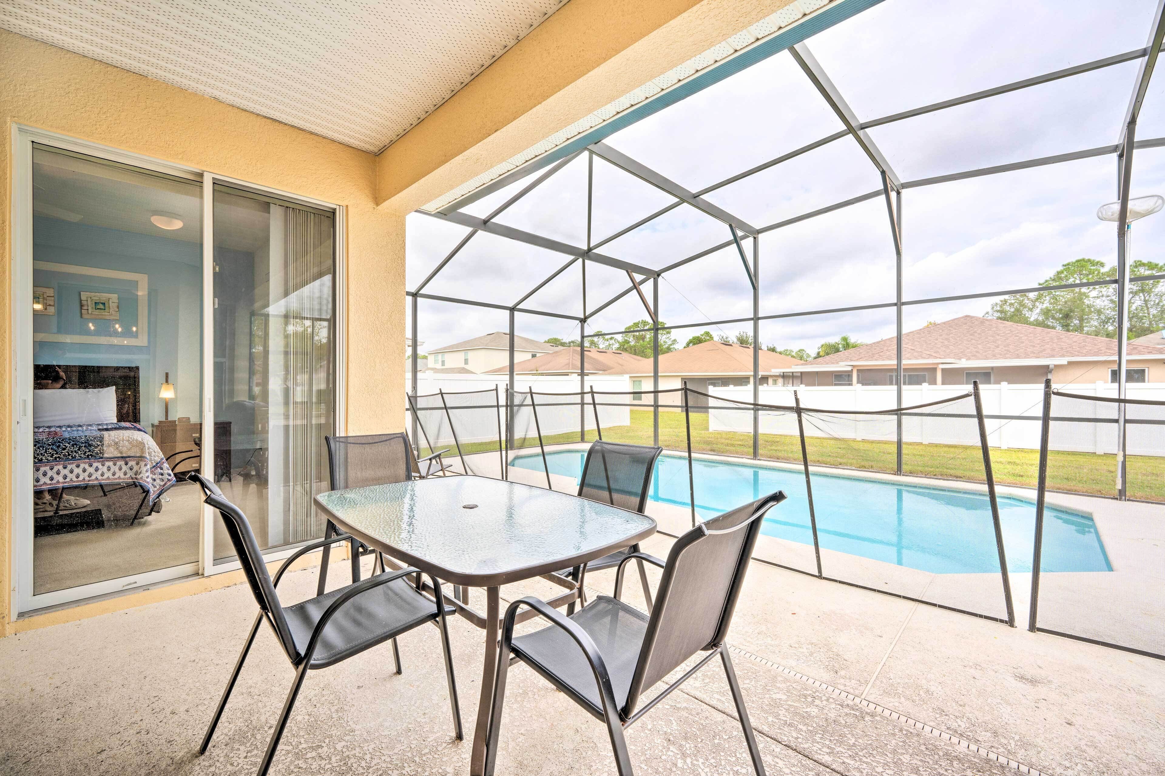 An outdoor patio with a glass-enclosed pool, a table with chairs, and a view of neighboring houses.
