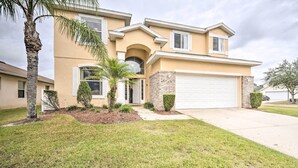 A two-story house with a garage, a front yard with grass and a palm tree, and a brick section on the side. - Dog-friendly Kissimmee Home w/ Lanai + Pool! (Kissimmee)
