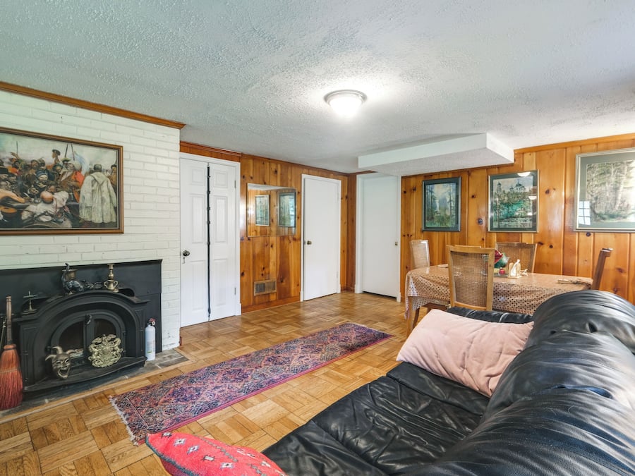 A living room with a fireplace, a black leather sofa, a patterned rug, and wooden walls.