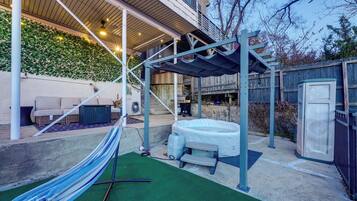 A backyard with a hammock, a hot tub, and a covered patio area.