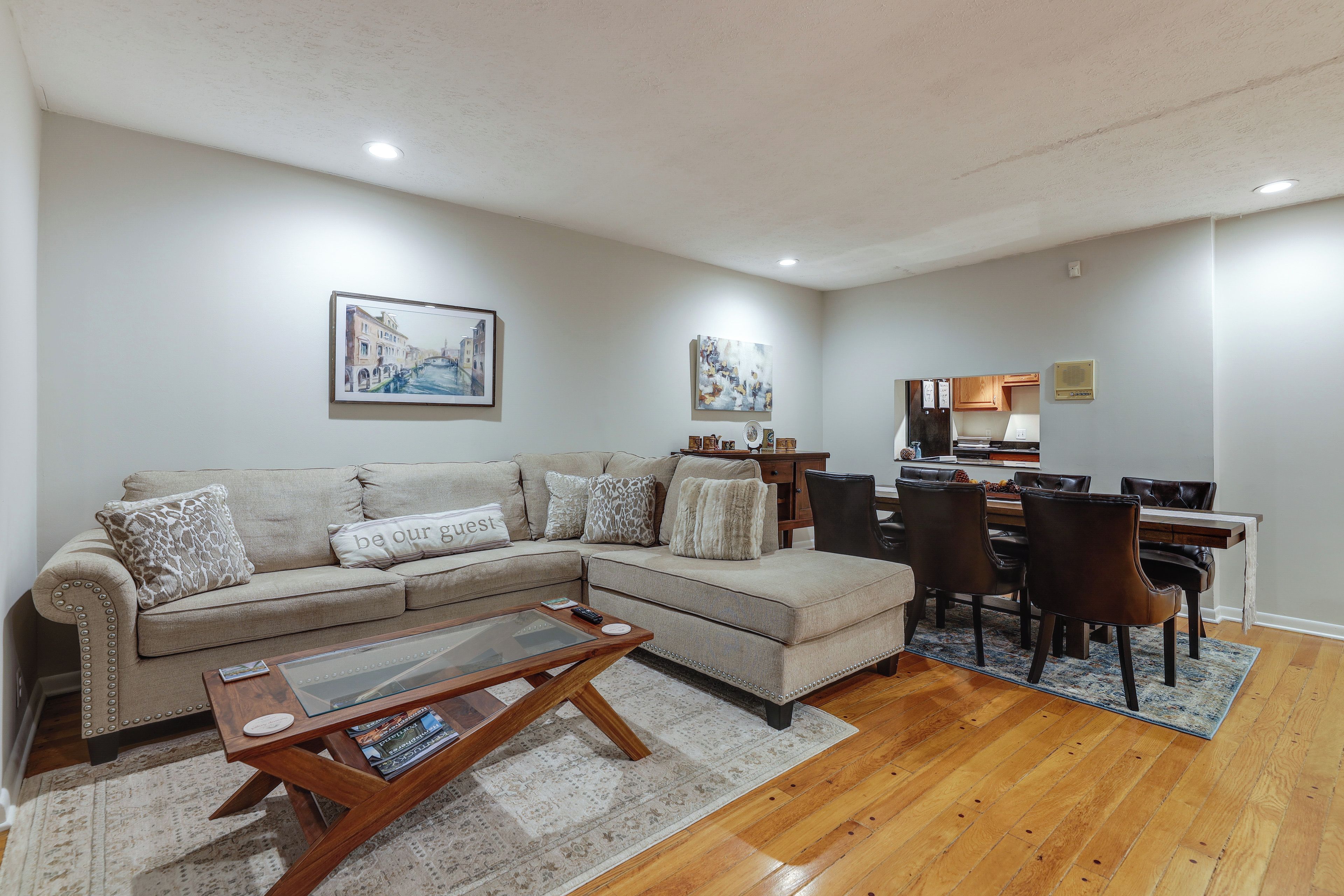 A living room with a beige sectional sofa, a glass coffee table, and a dining area with a wooden table and chairs.