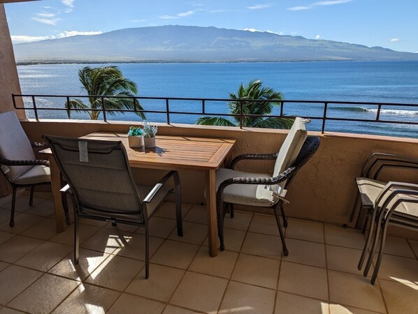A balcony with a table and chairs, overlooking a body of water and mountains. - Best view in Maui. Condo fully remodeled. (Wailuku)
