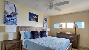 Een slaapkamer met een bed, twee nachtkastjes, een plafondventilator en kunstwerken aan de wanden.