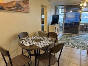 A dining area with a round table, four chairs, a television on a cabinet, and a view of the ocean through a glass door. - Best view in Maui. Condo fully remodeled. (Wailuku)