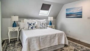 A bedroom with a skylight, a bed with patterned pillows, two bedside tables with lamps, a rug, and a painting on the wall. - Martha's Vineyard Escape Near South Beach (Edgartown)