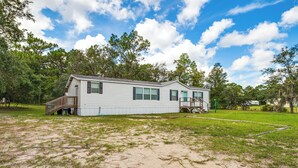 A single-story mobile home with a deck and a small porch, surrounded by a grassy yard and trees. - 5 Mi to Homosassa Springs Park: Home w/ Yard! (Homosassa)