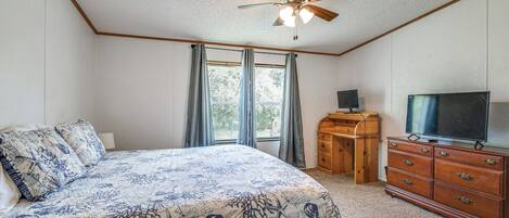 A bedroom with a bed, a ceiling fan, a dresser, a TV, and a window with curtains.