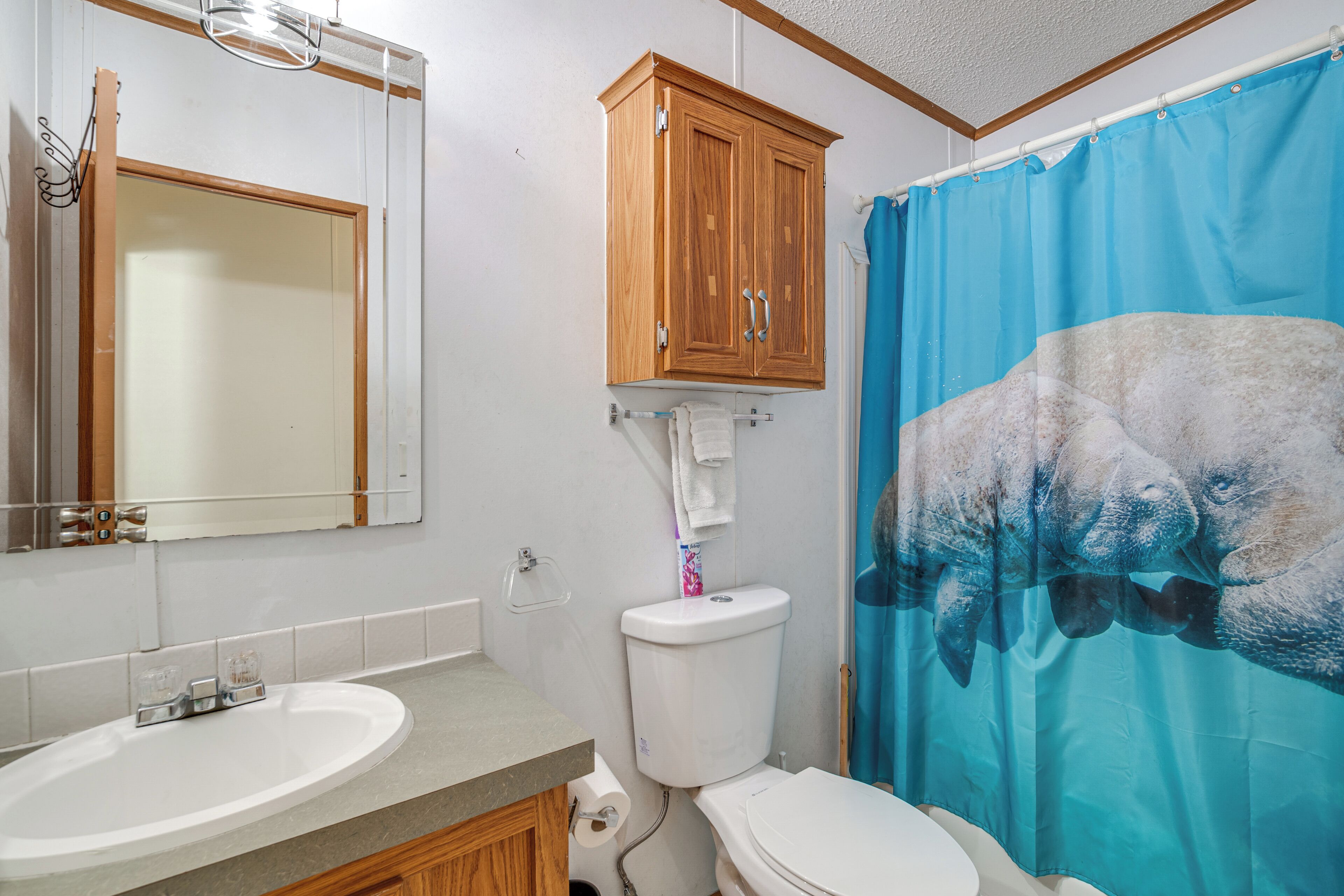 A bathroom with a wooden cabinet, a sink, a toilet, and a blue shower curtain.
