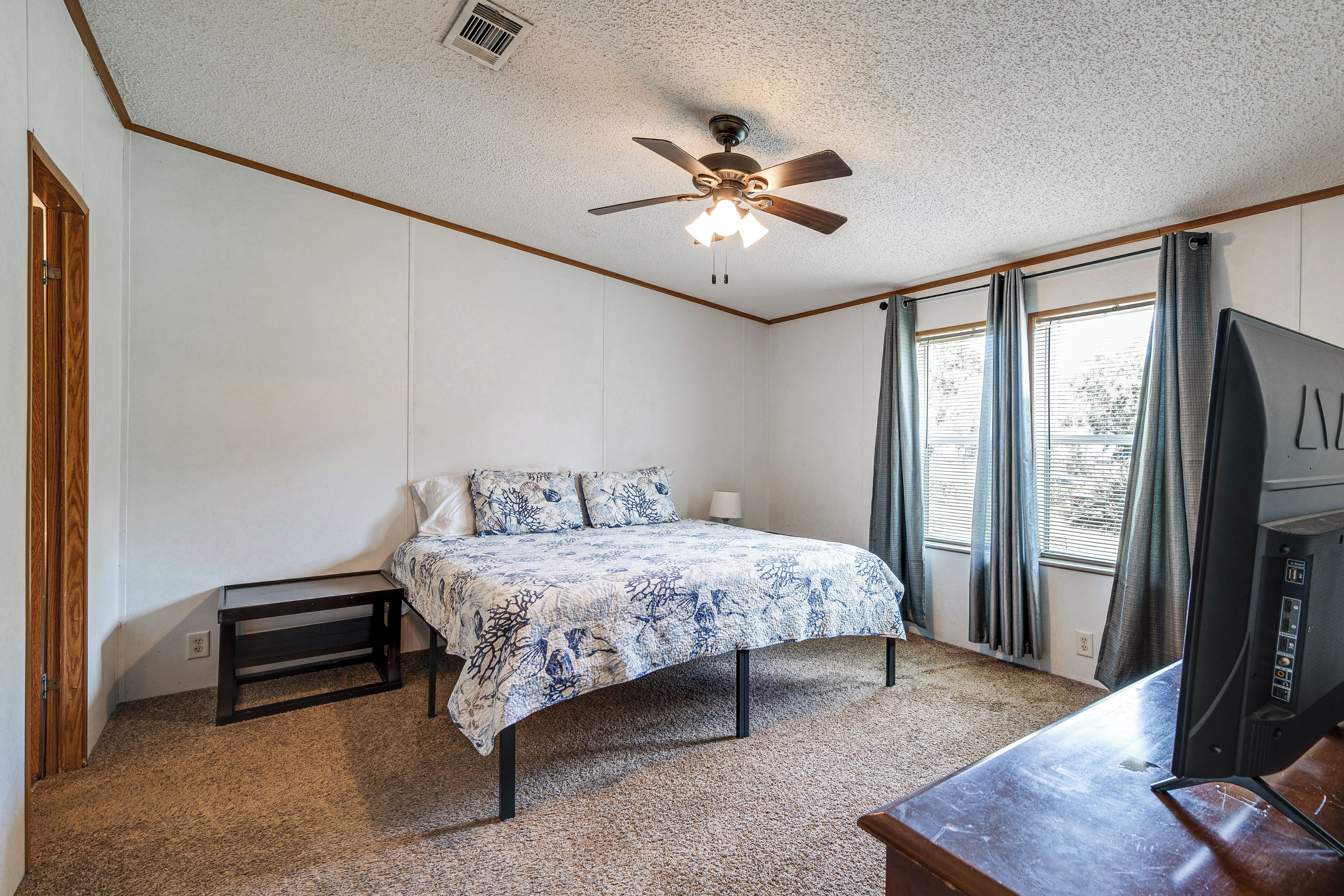 A bedroom with a bed, a ceiling fan, a window with curtains, and a television.