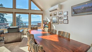 Une pièce spacieuse avec une grande table en bois, des chaises à motifs, un canapé en cuir et une vue sur la mer grâce à de grandes fenêtres.