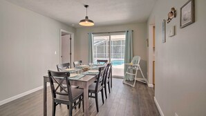 Comedor con una mesa preparada para cuatro, ventilador de techo y vista a una piscina a través de amplios ventanales.