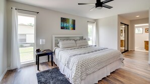 A modern bedroom with a large bed, a ceiling fan, a painting, and a view of the outdoors. - Walk to Lake: Geataway w/ Yard in Inverness (Inverness)