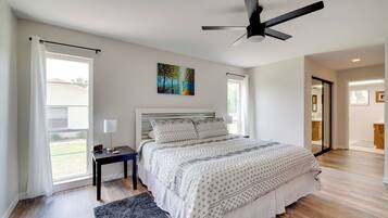 A modern bedroom with a large bed, a ceiling fan, a painting, and a view of the outdoors.