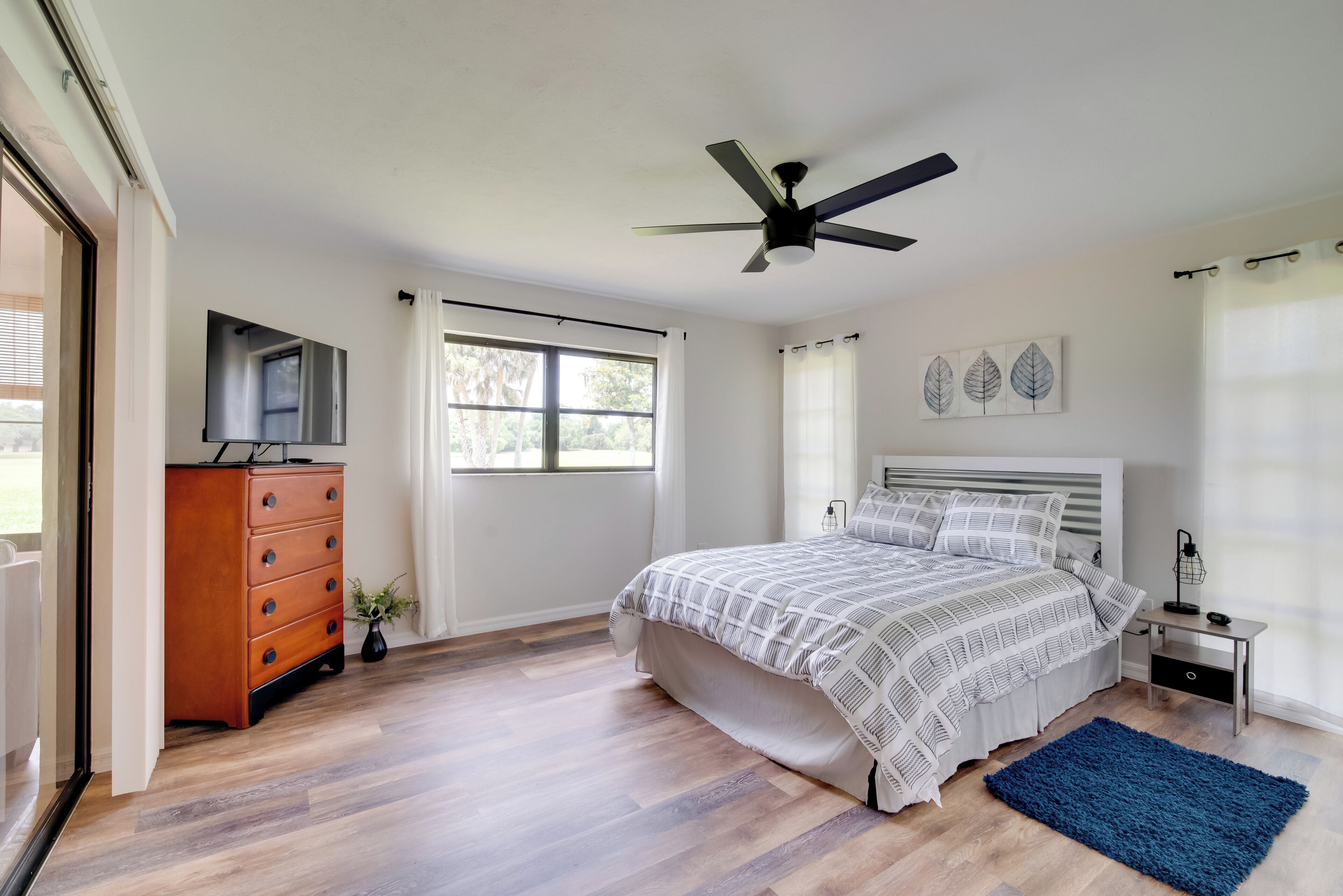 A bedroom with a bed, dresser, ceiling fan, and a window.