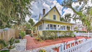 A yellow house with a white picket fence, surrounded by a garden with various plants and a brick pathway. - Historic Green Cove Springs Home - Walk to Coast! (Green Cove Springs)