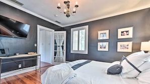 A bedroom with a bed, a desk, a TV, and a chandelier. - Historic Green Cove Springs Home - Walk to Coast! (Green Cove Springs)