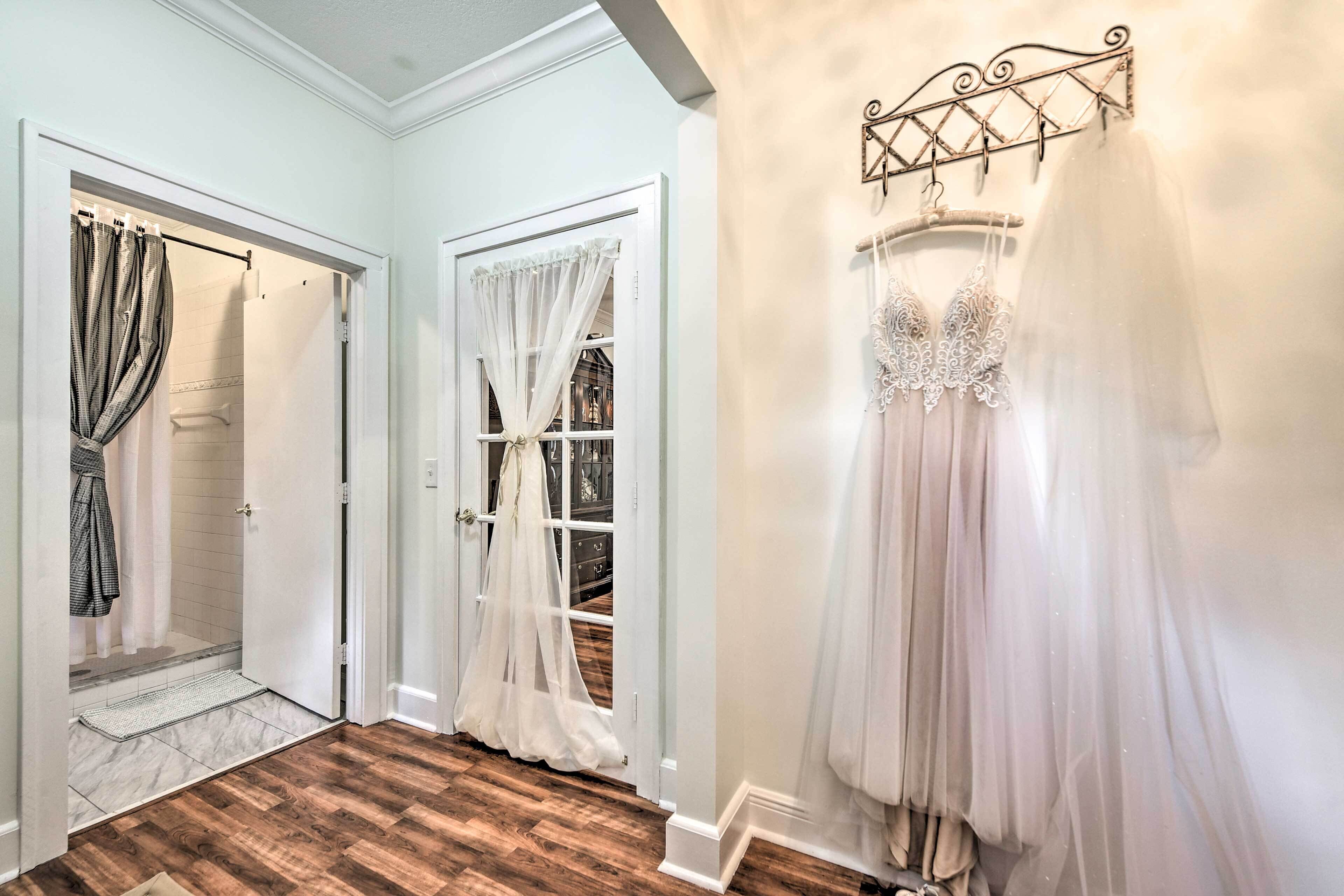 Un pasillo con suelo de madera, una ducha con cortina y un vestido de novia en un perchero de pared.