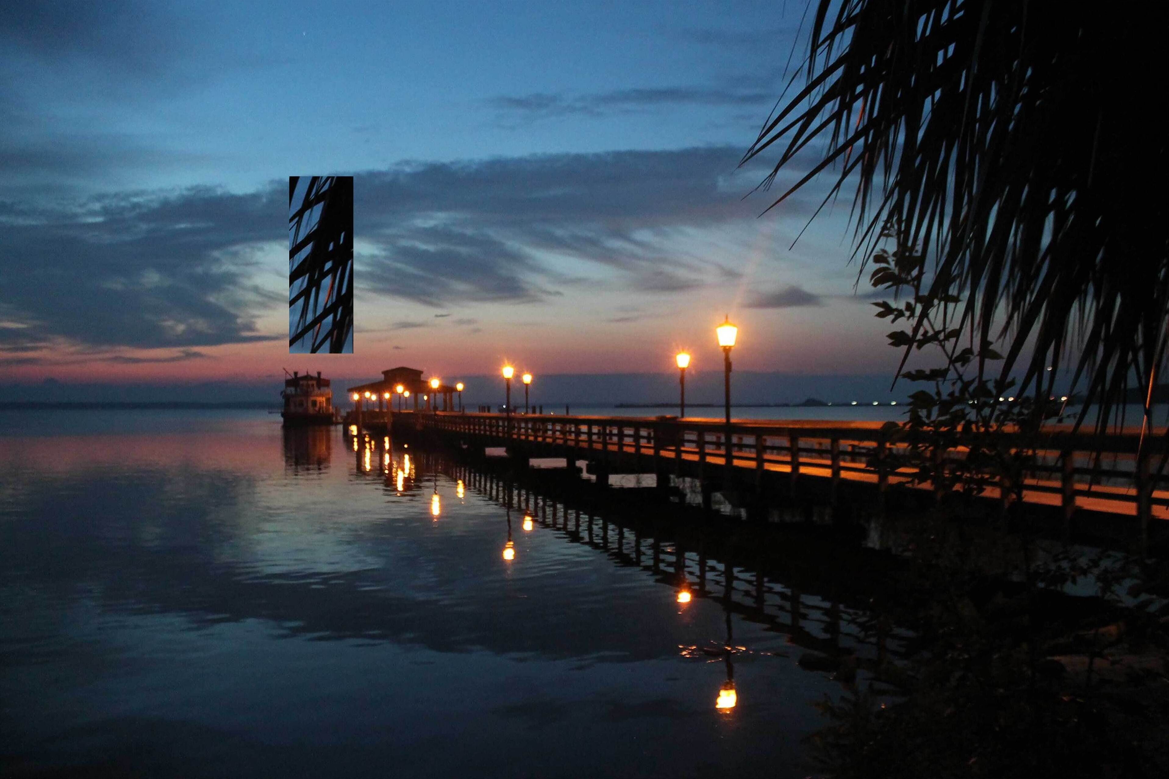 A pier extending into calm water at dusk with street lamps along its length.