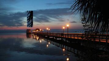 A pier extending into calm water at dusk with street lamps along its length.