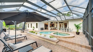 Un espacio al aire libre cubierto con piscina, sillas de descanso y una mesa de patio.