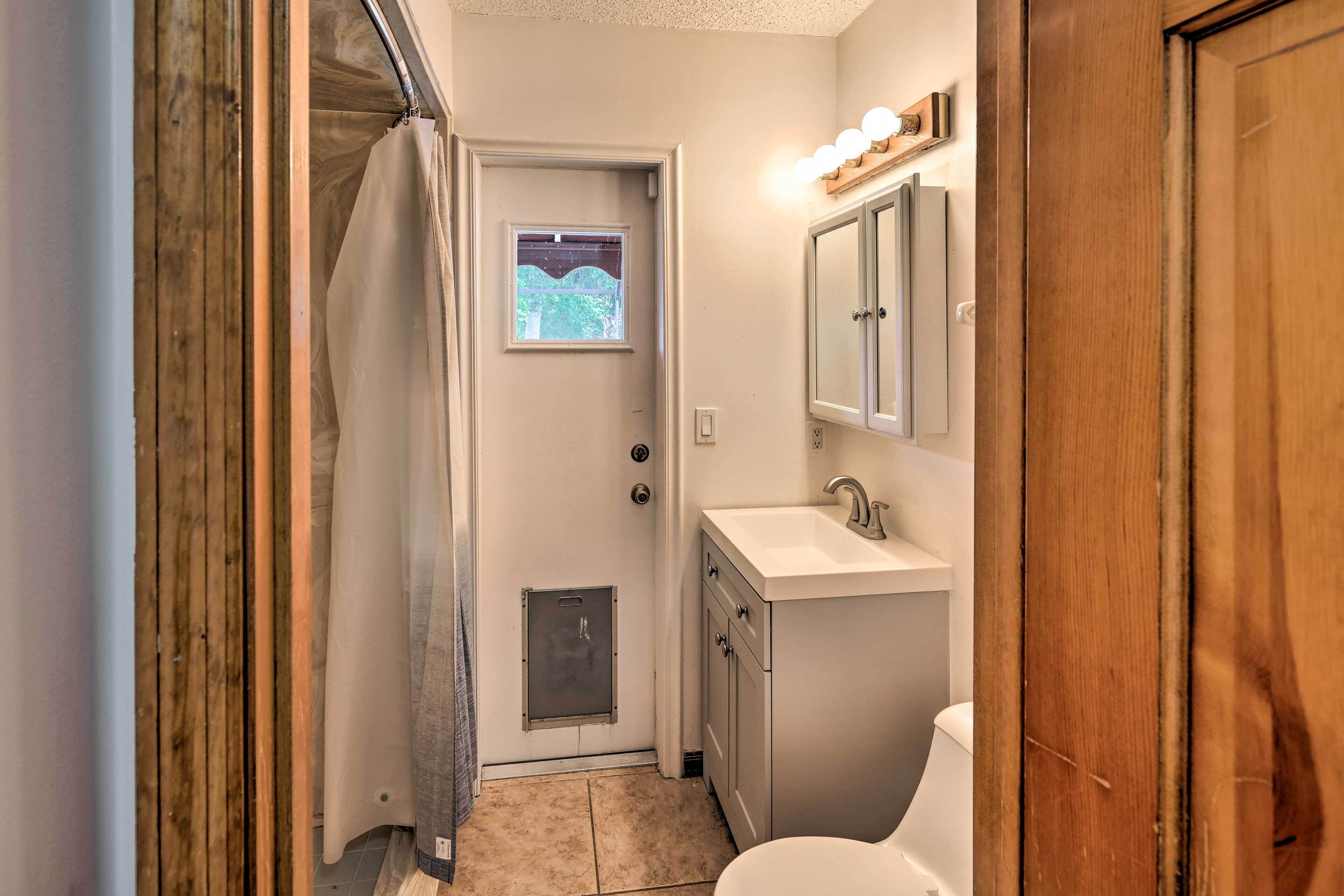 A narrow bathroom with a shower, a toilet, and a vanity with a mirror.