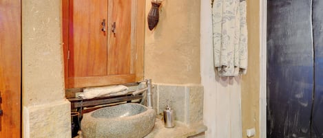 Un baño con lavamanos de piedra, armarios de madera y ventana con marco negro.