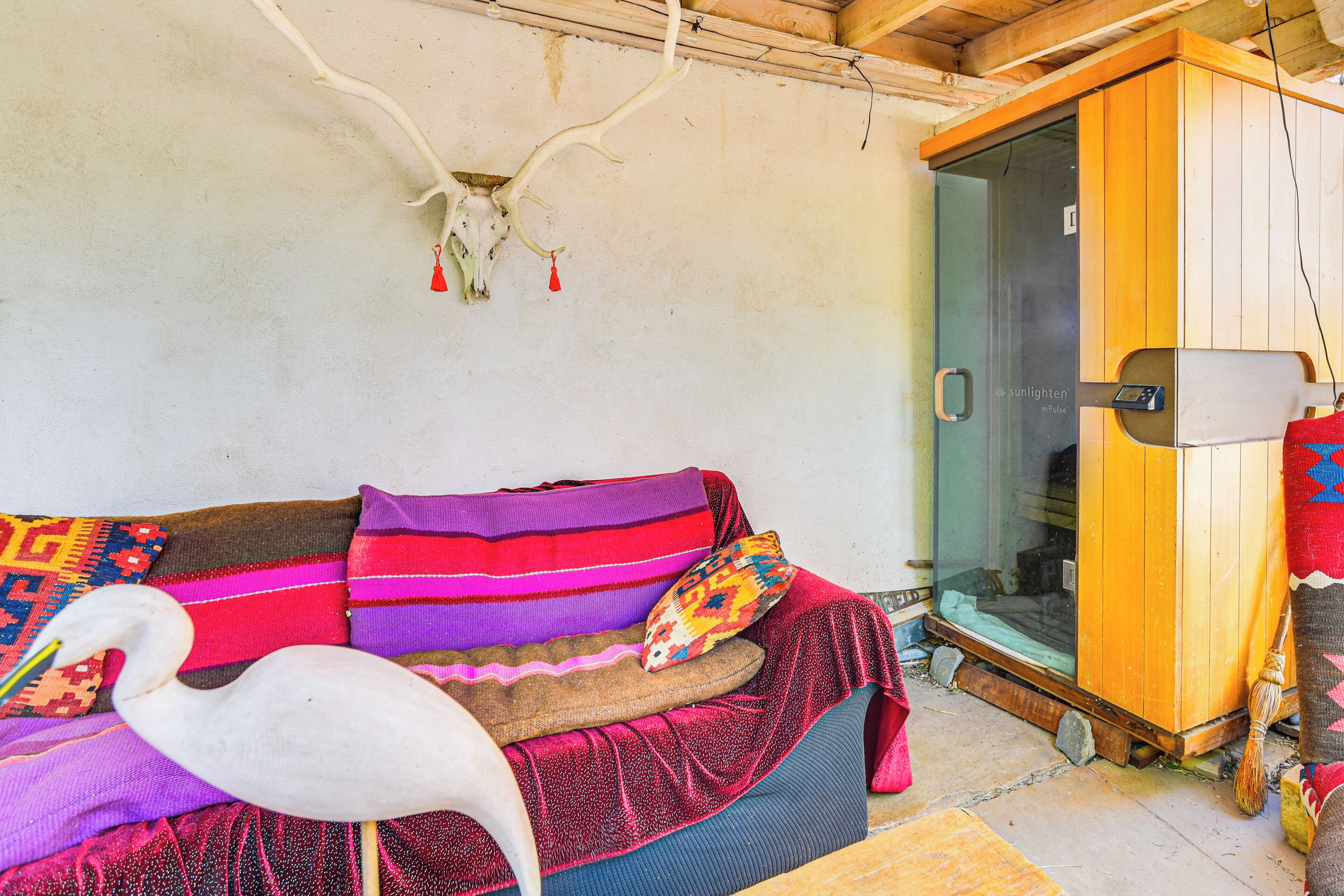 Een kamer met een houten plafond, een glazen deur, een houten garderobe en een kleurrijke bank met een decoratie van een witte vogel.