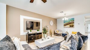 A modern living room with a flat-screen TV, a white coffee table, and a beige sofa. - Central Family Home w/ Lanai < 10 Mi to Disney! (Davenport)