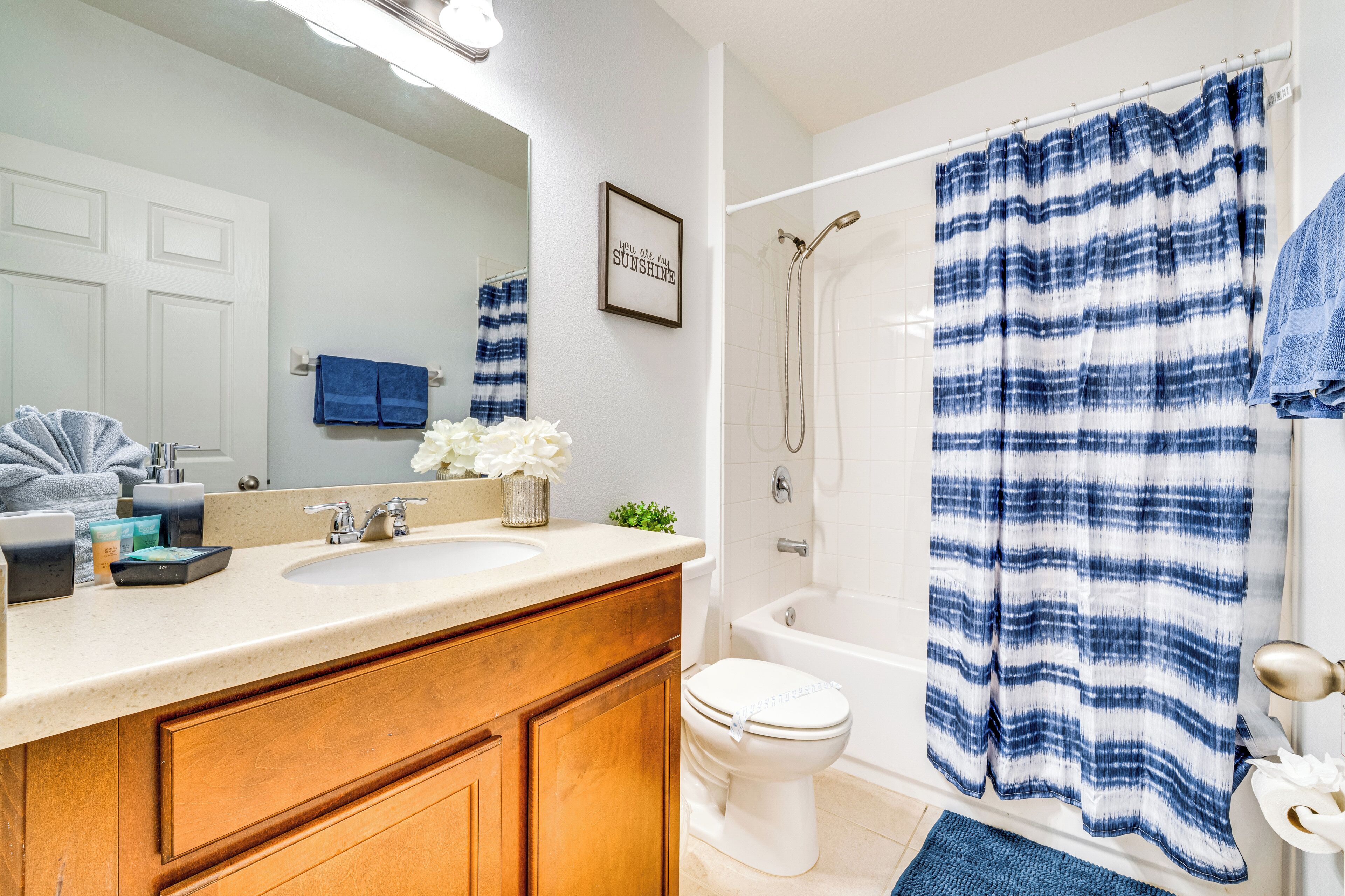 Un bagno con un lavandino bianco, un mobile bagno in legno, un WC, una doccia e un tenda da doccia a righe blu e bianche.