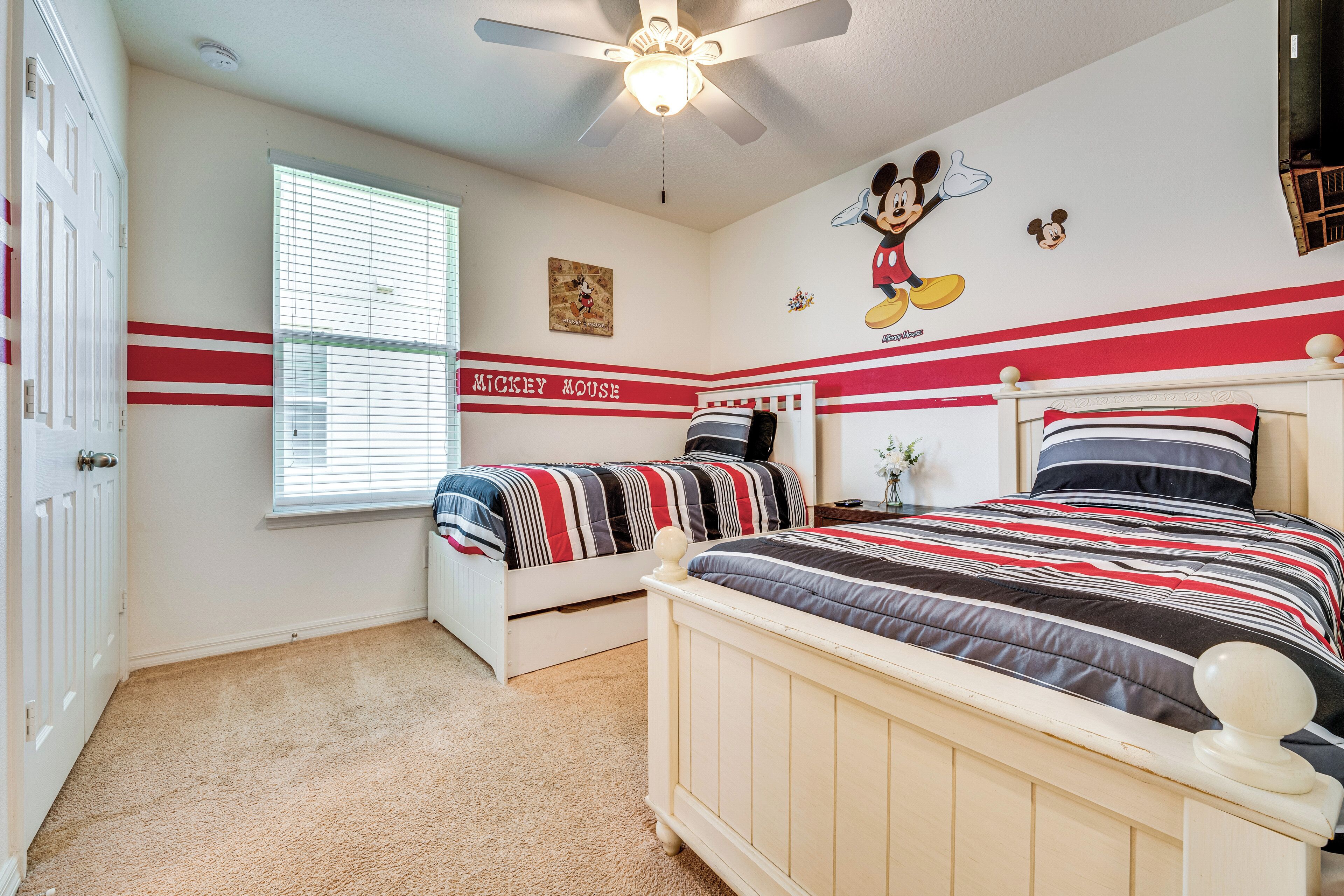 Ein Schlafzimmer mit zwei Betten, einer Wandmalerei von Mickey Mouse und einem Fenster mit Jalousien.