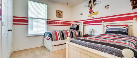 Ein Schlafzimmer mit zwei Betten, einer Wandmalerei von Mickey Mouse und einem Fenster mit Jalousien.