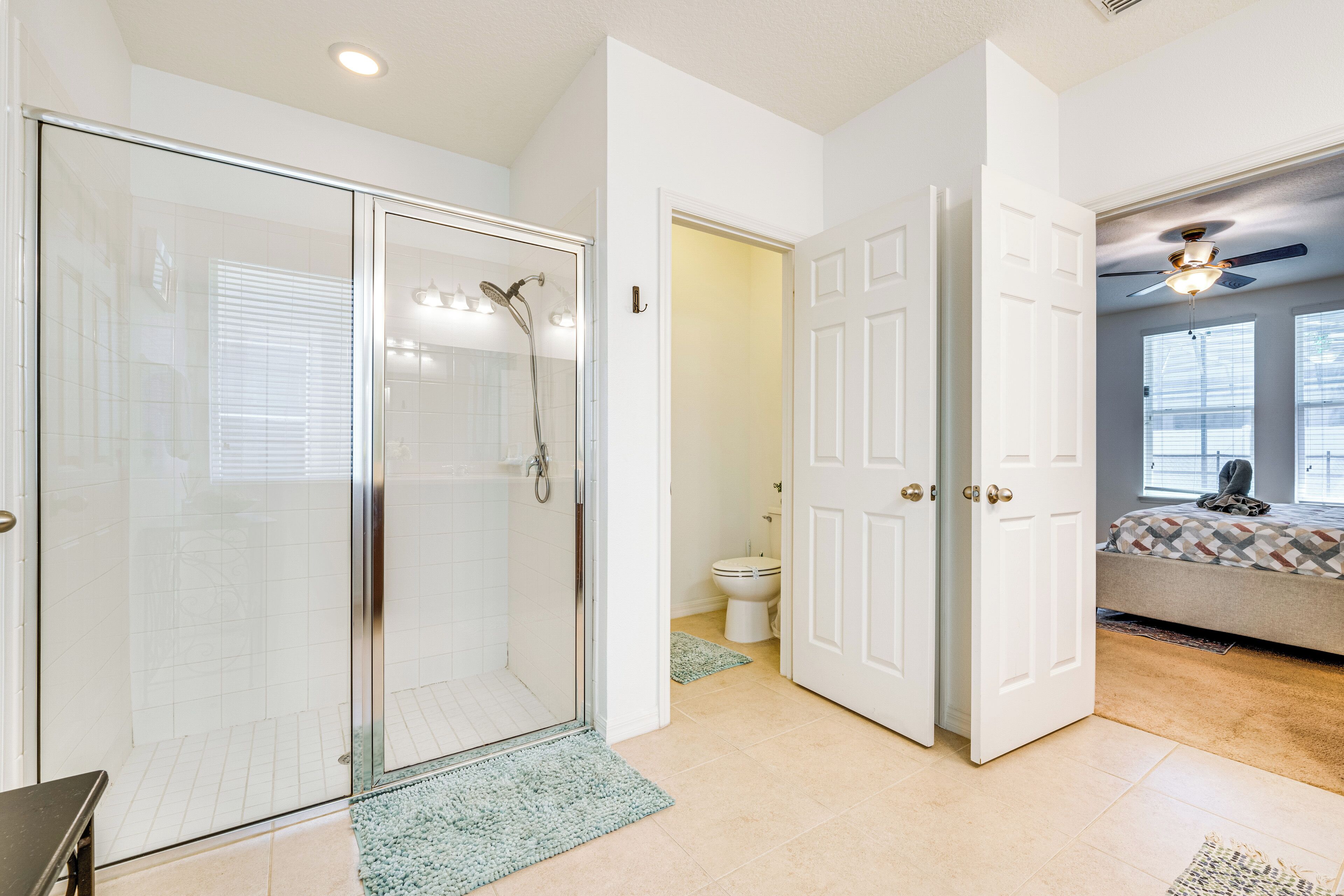 A modern bathroom with a glass shower enclosure, a toilet, and a bed in the adjacent room.