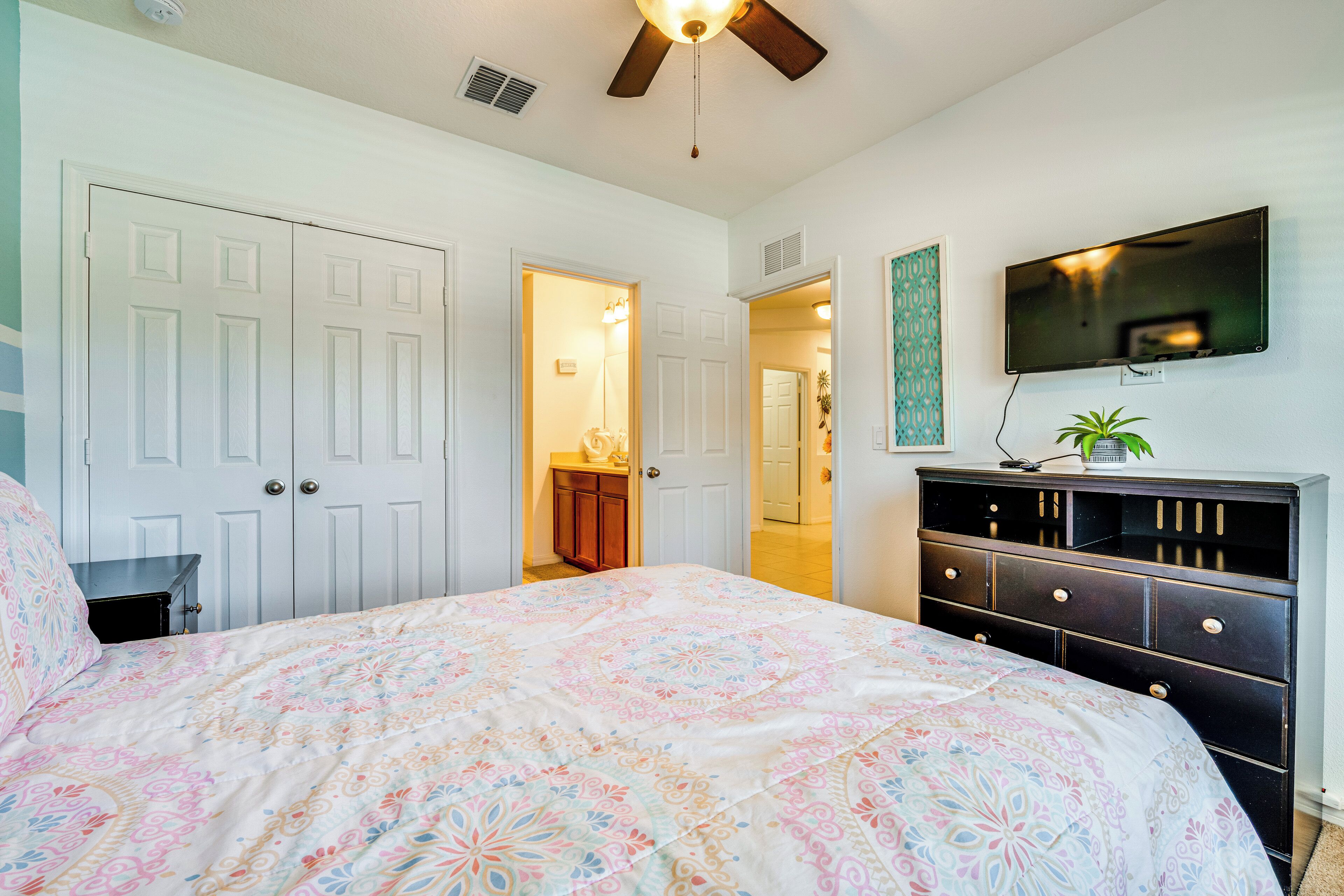 A bedroom with a bed, a dresser, a ceiling fan, and a TV mounted on the wall.