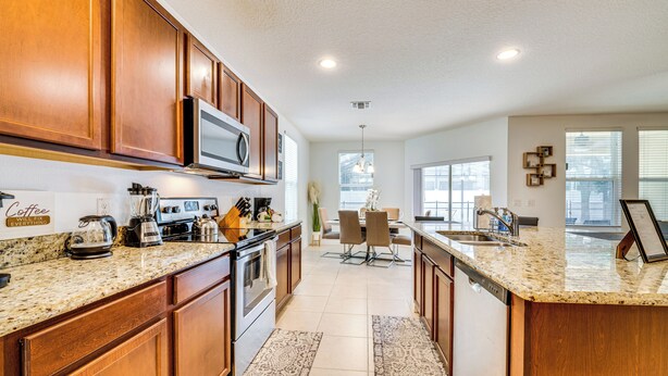 A modern kitchen with wooden cabinets, granite countertops, and stainless steel appliances. There is a dining area with a table and chairs. - Central Family Home w/ Lanai < 10 Mi to Disney! (Davenport)