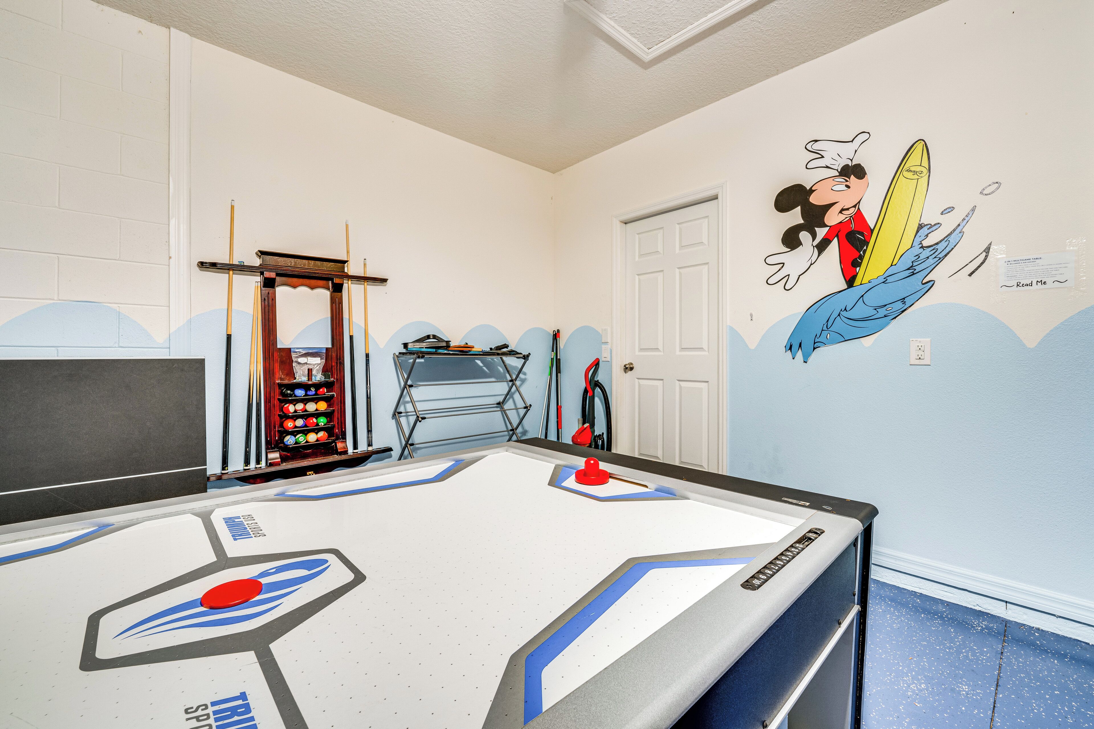 A pool table with a unique design, a dartboard, and a wall mural of a cartoon character surfing.