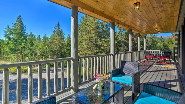 Eine Holzterrasse mit Gartenmöbeln und Geländer, mit Blick auf ein bewaldetes Gebiet.