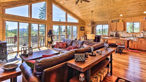 A cabin interior with a large wooden ceiling, a cozy living area with a leather sofa, a dining table, and a kitchen area with wooden cabinets. - Jefferson Cabin w/ Fire Pit: Near Hiking Trails! (Como)