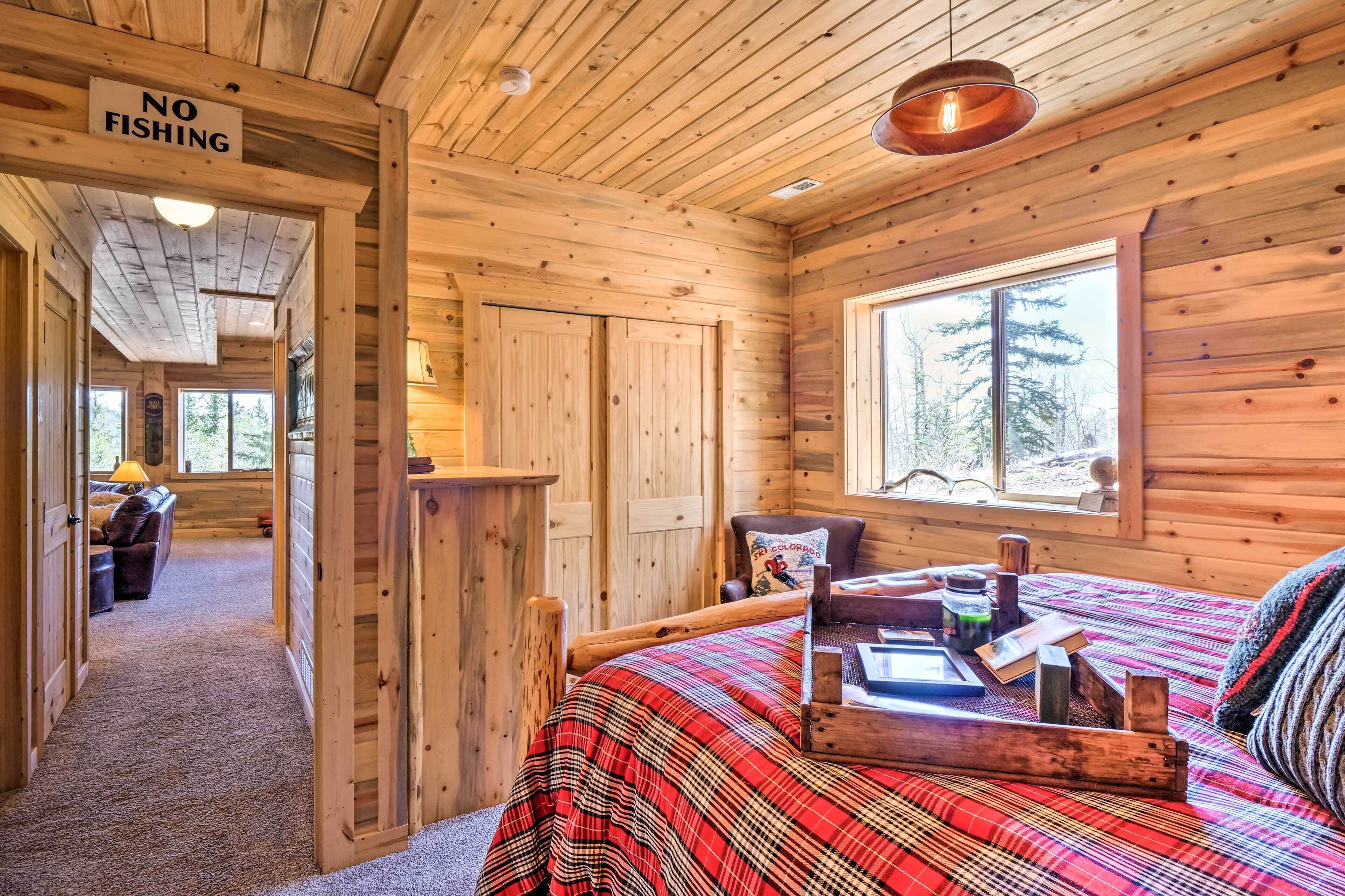 A wooden cabin interior with a bed, a 'NO FISHING' sign, a window with a forest view, and a cozy atmosphere.