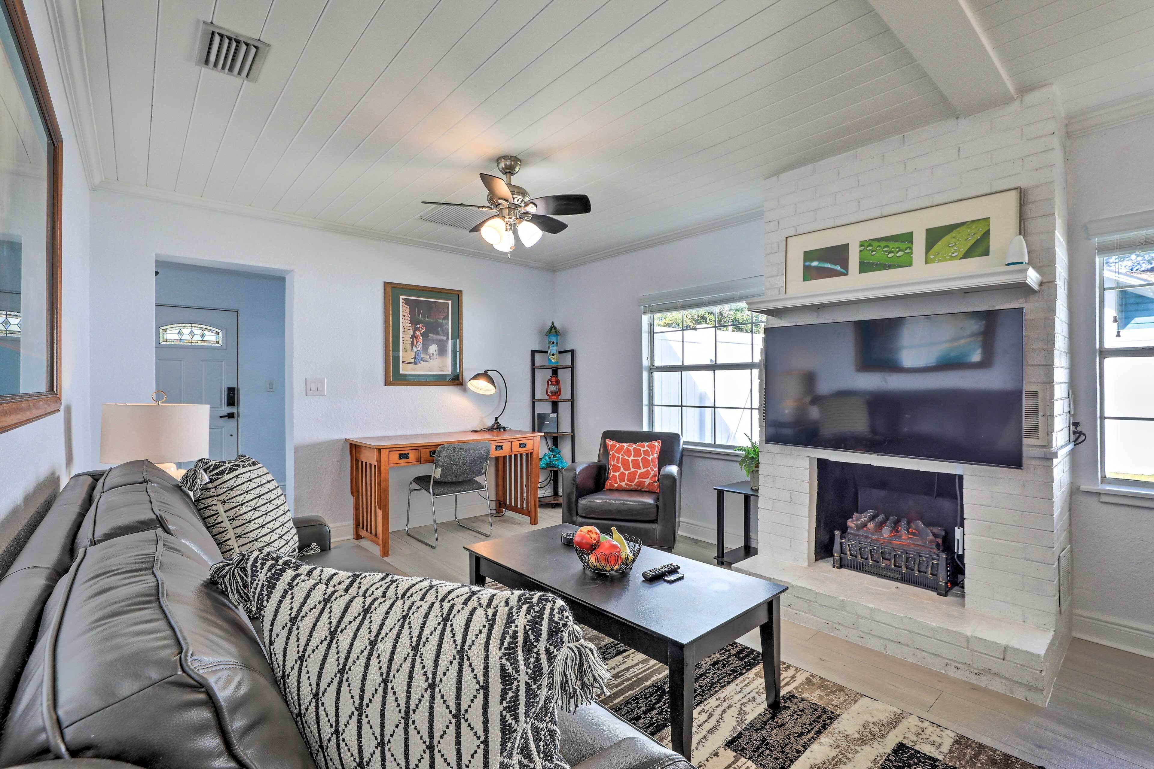A living room with a sofa, a coffee table, a fireplace, a TV, and a desk.