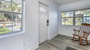 A room with a white door, large windows, a rocking chair, and a patterned rug. - Pet-friendly Mt Dora Home w/ Fire Pit & Patio (Mount Dora)