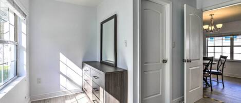 A spacious room with a large window, a built-in wooden dresser, and a dining area with a chandelier.
