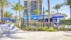 A hotel with outdoor seating, palm trees, and a pool area. - Sunny Ocean Village Beach Condo: Community Pool (Fort Pierce)